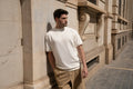 Man tegen een stenen gevel in een gebroken wit Freedom Fit Tee met een beige pantalon